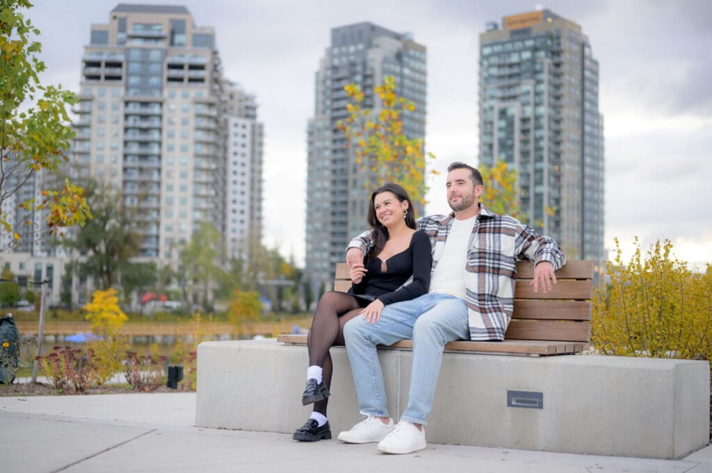 Engaged couple holding hands near historic bridge in Waterloo Park with buildings in the background
