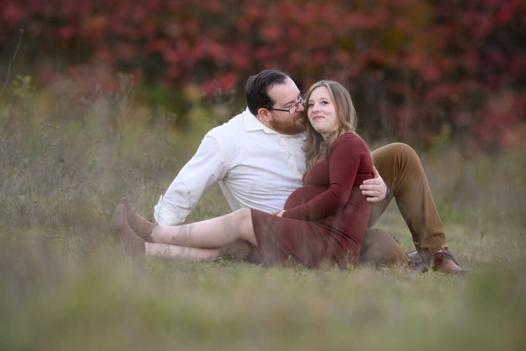 Couple posing on the boardwalk at Huron Natural Area surrounded by tall trees and autumn colors